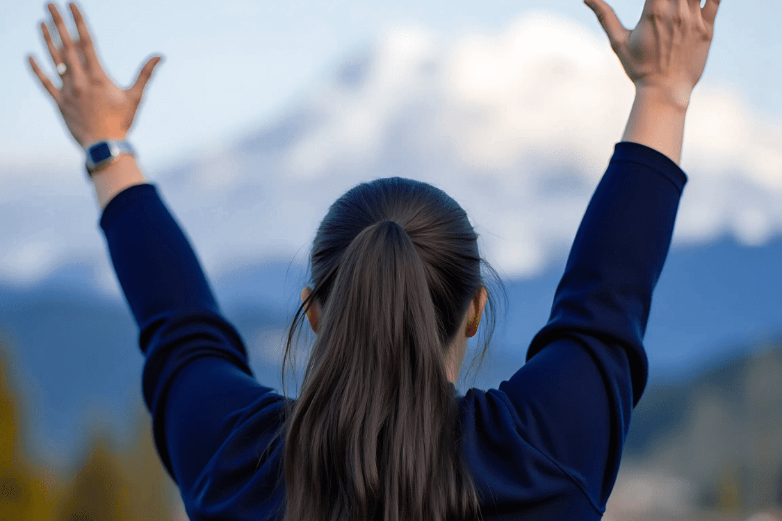 Christian woman worshiping in nature with raised arms, surrendering to God.
